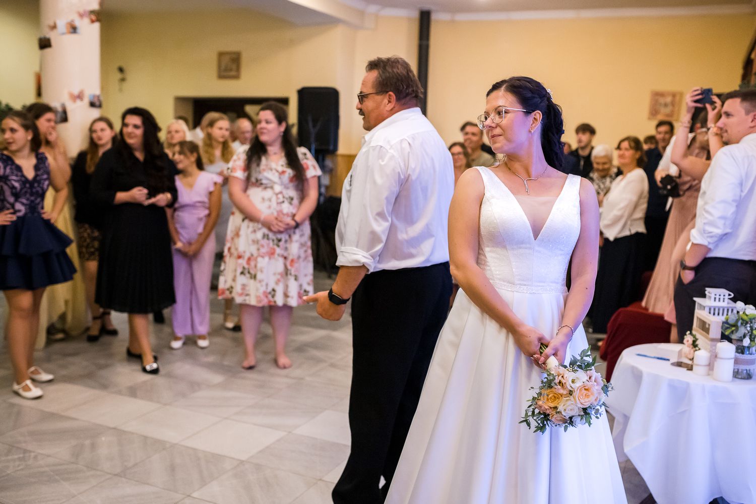 Guests mingle and dance at an elegant wedding reception with pink and white decor elements.