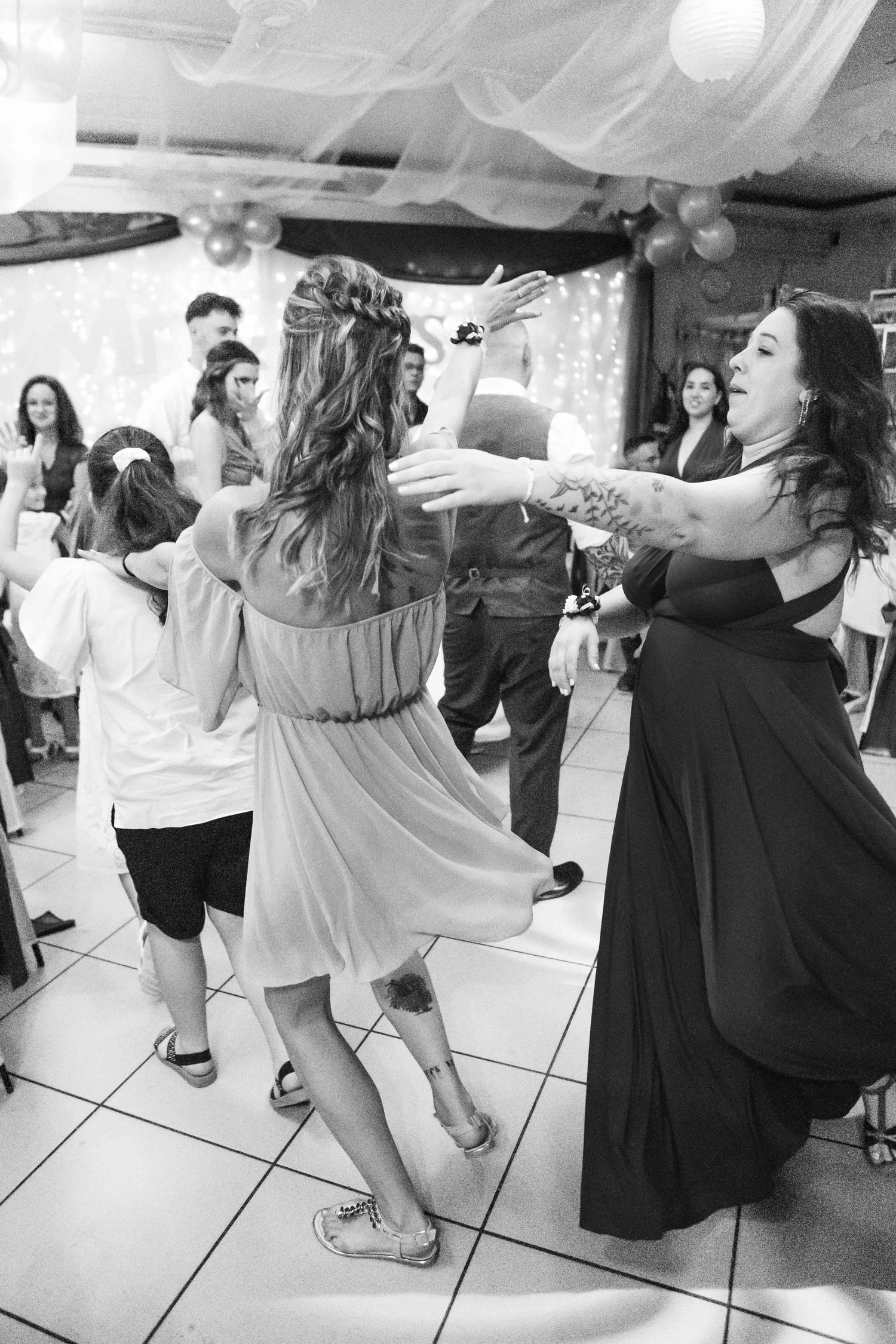 People dancing energetically at a party on a white tiled floor in black and white dresses.