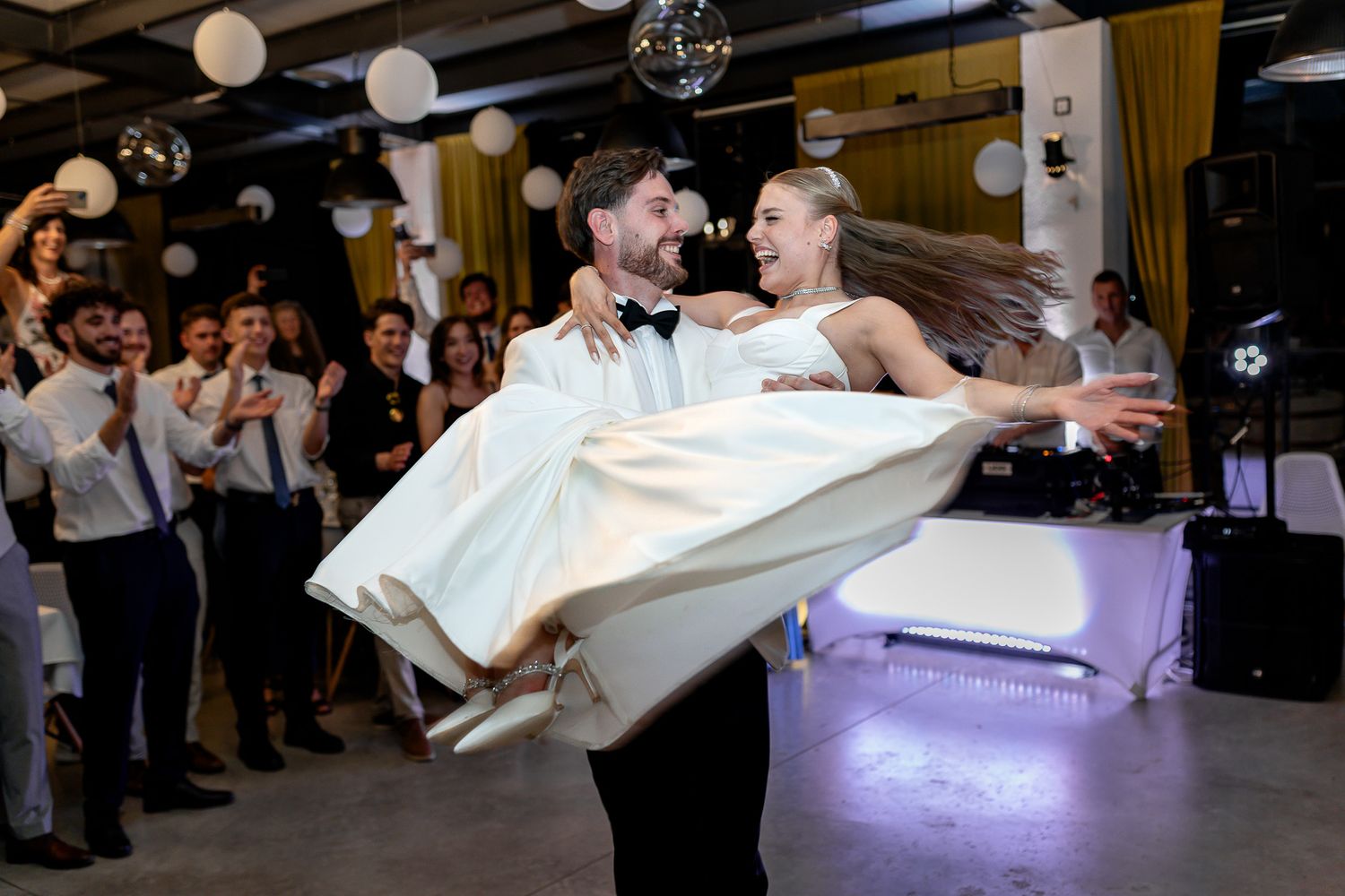 Couple performs dramatic dip during wedding dance as guests watch from the sidelines.