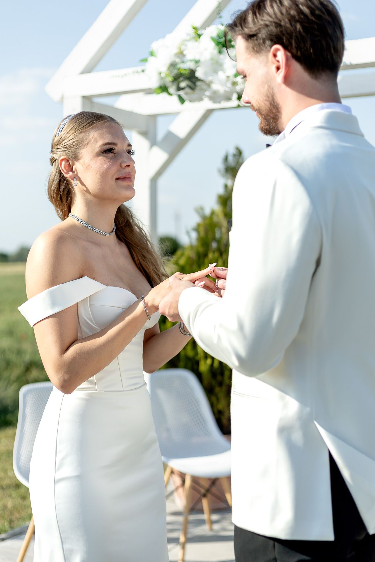 Wedding couple shares intimate first dance moment in white attire against natural outdoor backdrop.