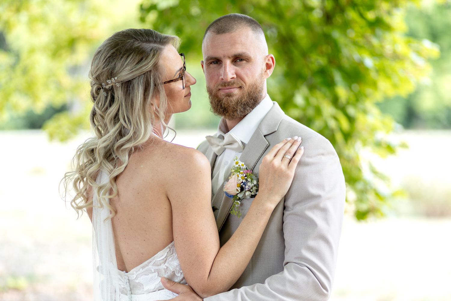 Newlyweds share a tender embrace in a garden setting with lush greenery.