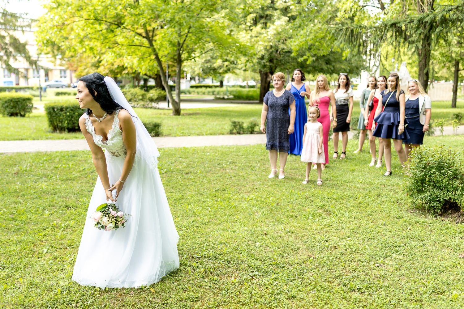 Wedding party members walk across a lush green lawn during an outdoor summer celebration.
