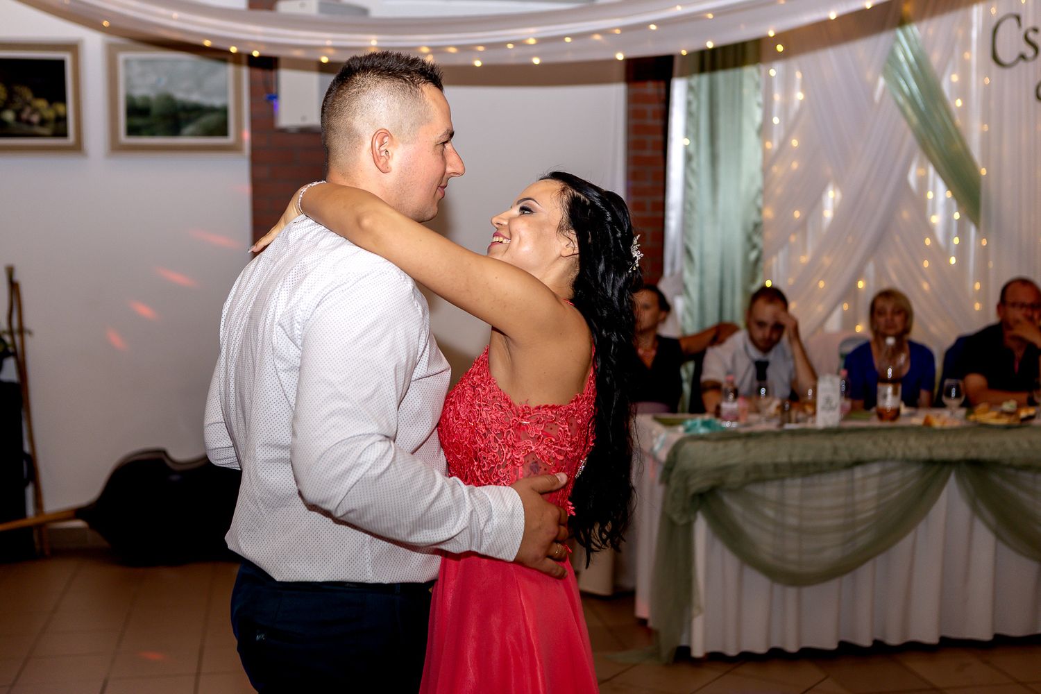 Couples dancing together at an elegant wedding reception with string lights and white decor in the background.