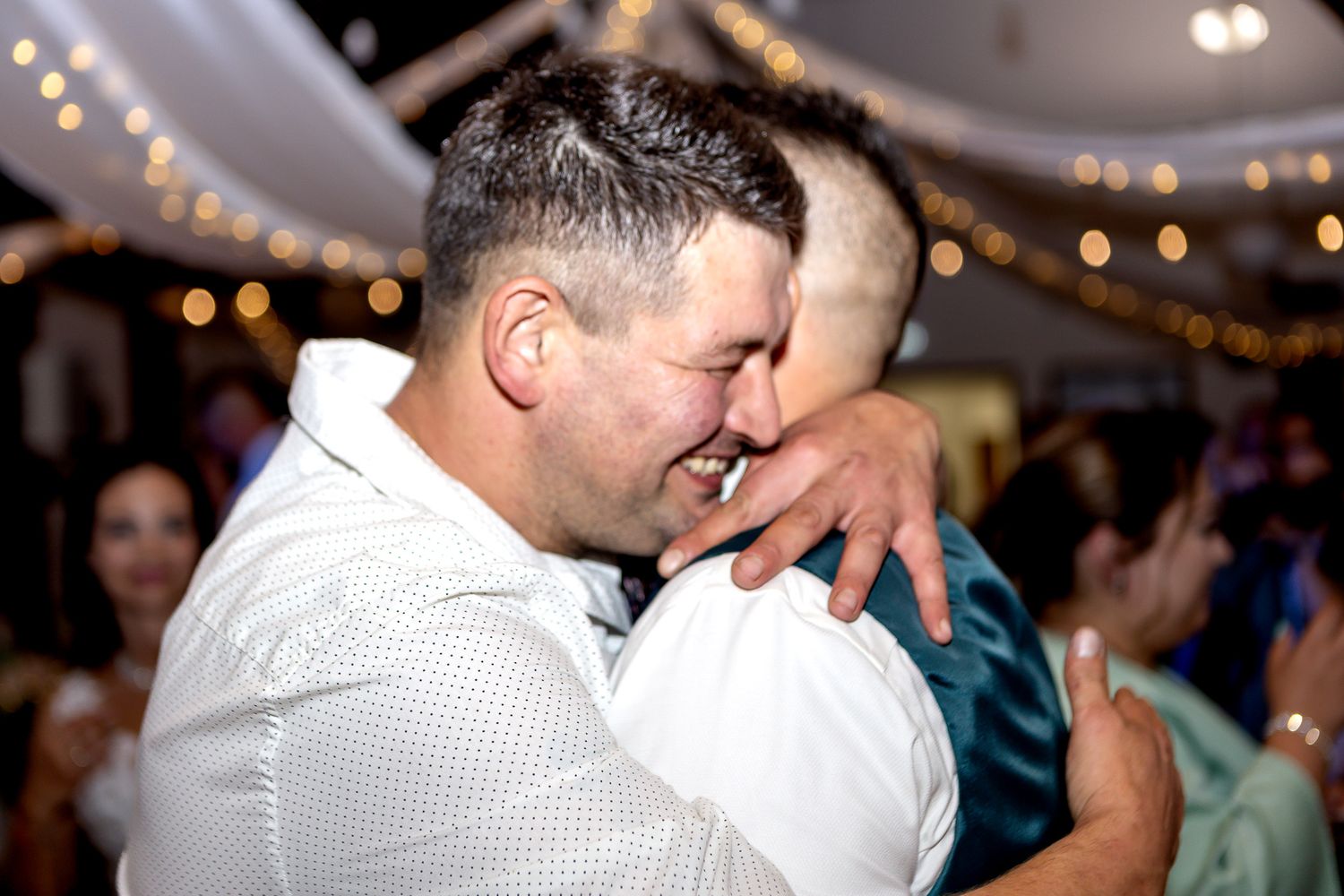 A couple shares a tender moment while dancing together at an indoor reception with twinkling lights overhead.