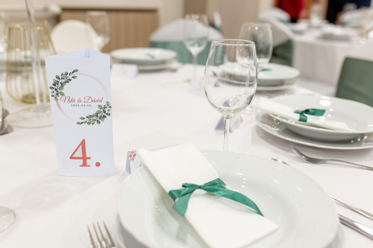 Elegant wedding reception table setting with white plates, wine glasses, and emerald green ribbon accents.