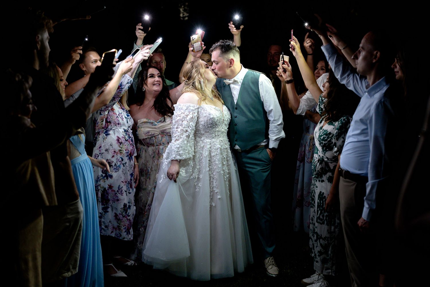 Wedding guests dance and celebrate on a dark dance floor during an evening reception celebration.