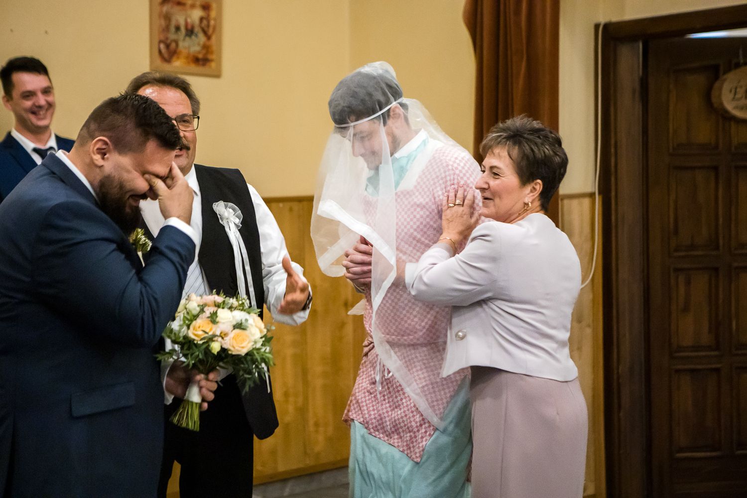Wedding party members embrace and celebrate during an emotional moment at an indoor reception venue.