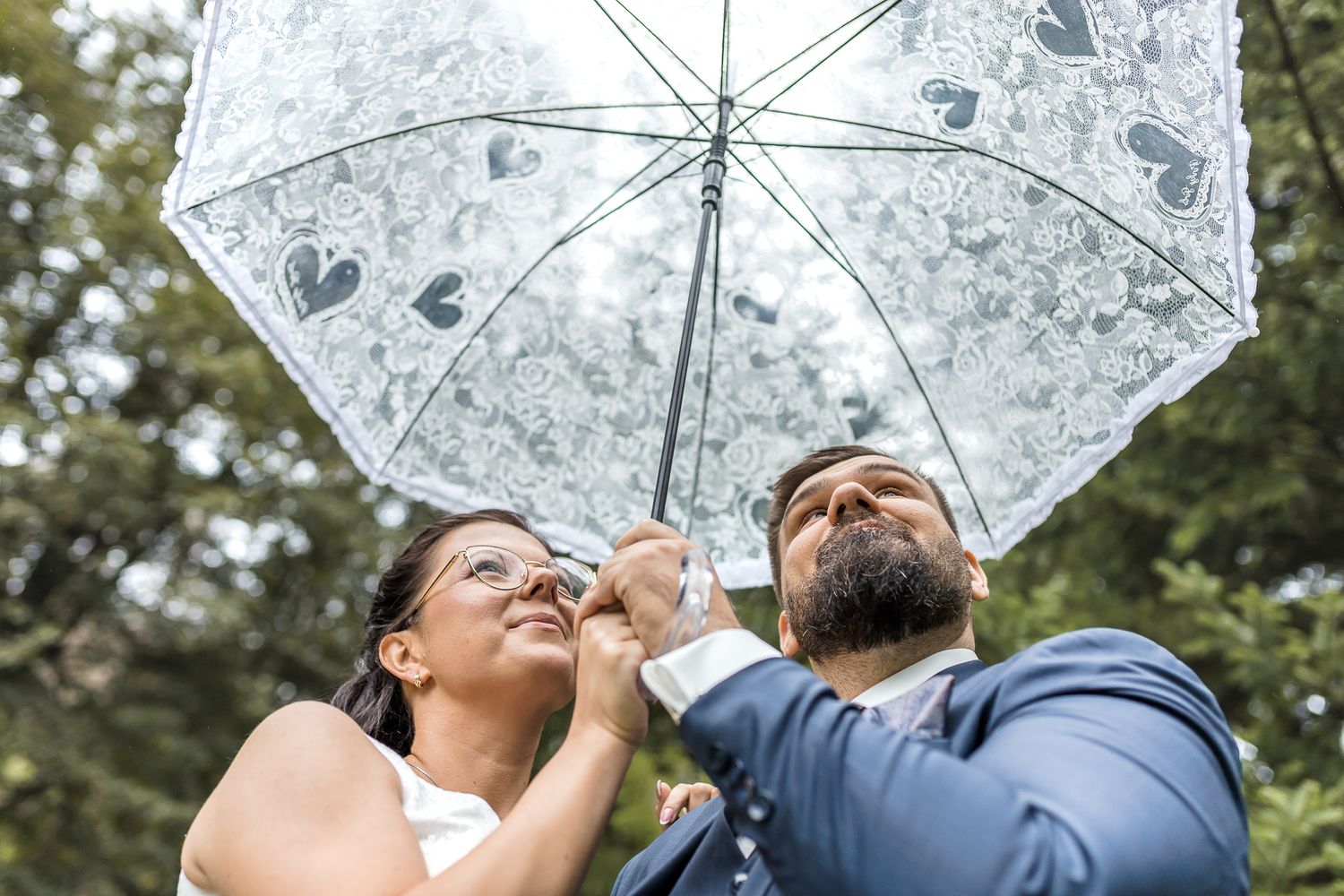 Two people hold a clear umbrella while looking up at the sky through it on a sunny day.