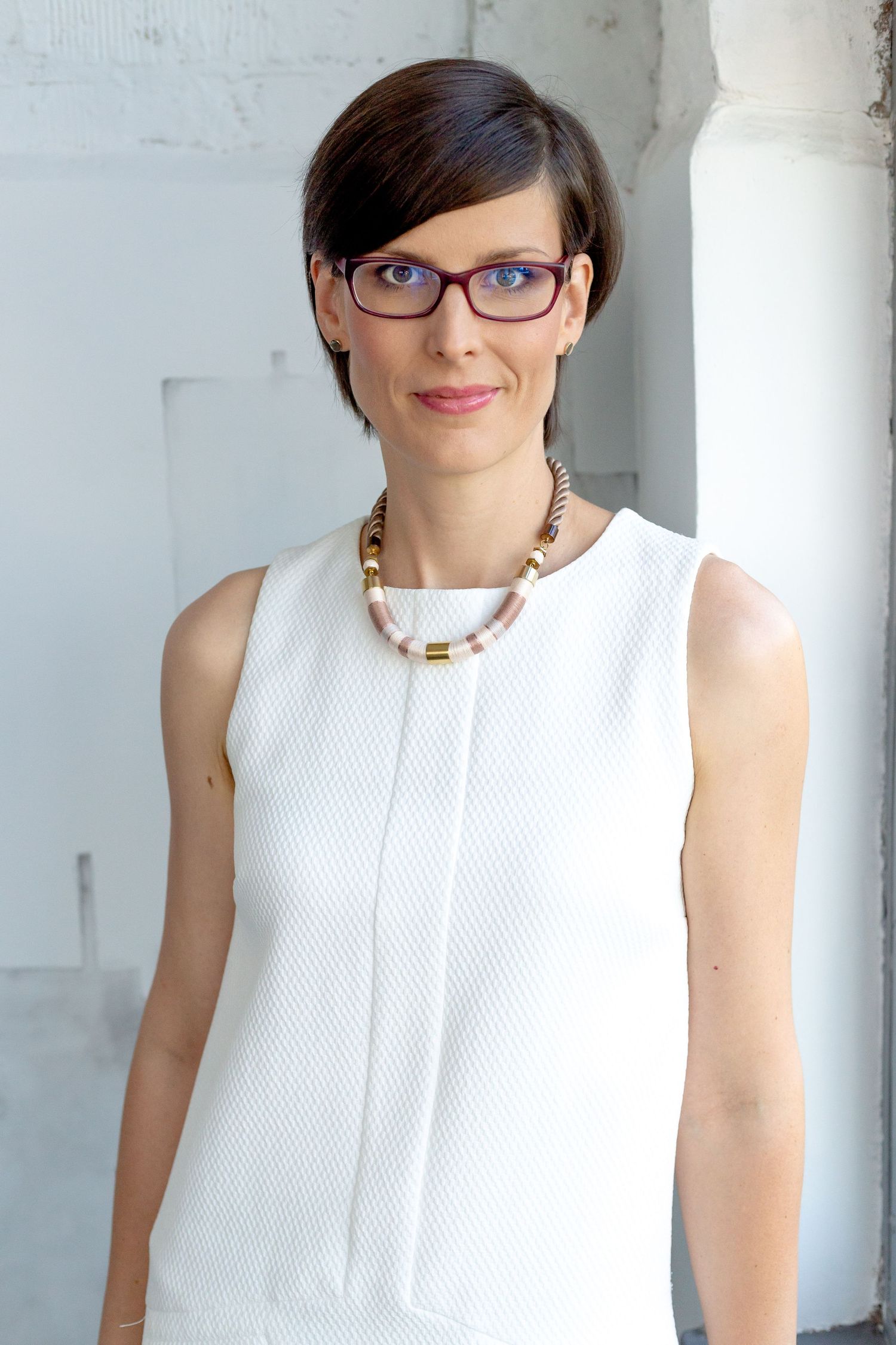 Professional headshot in a white sleeveless top with modern accessories and glasses.