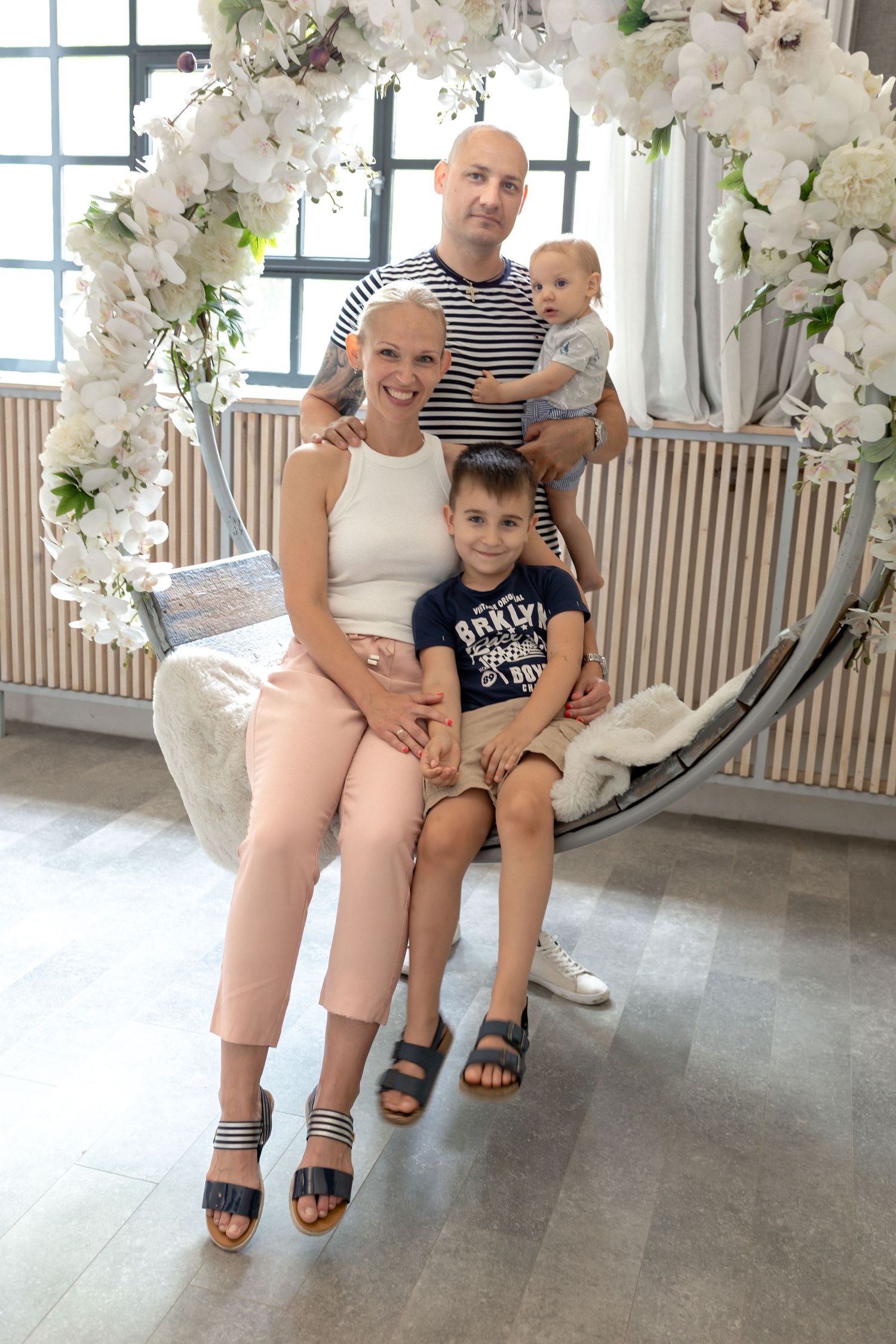 Family photoshoot in bright studio with white floral decorations and natural lighting.