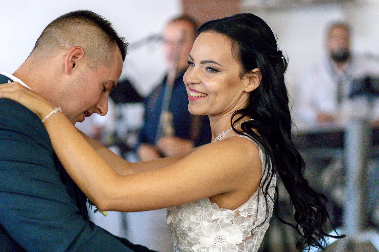 A couple dances together at their wedding reception, with the bride wearing a white gown and dark flowing hair.