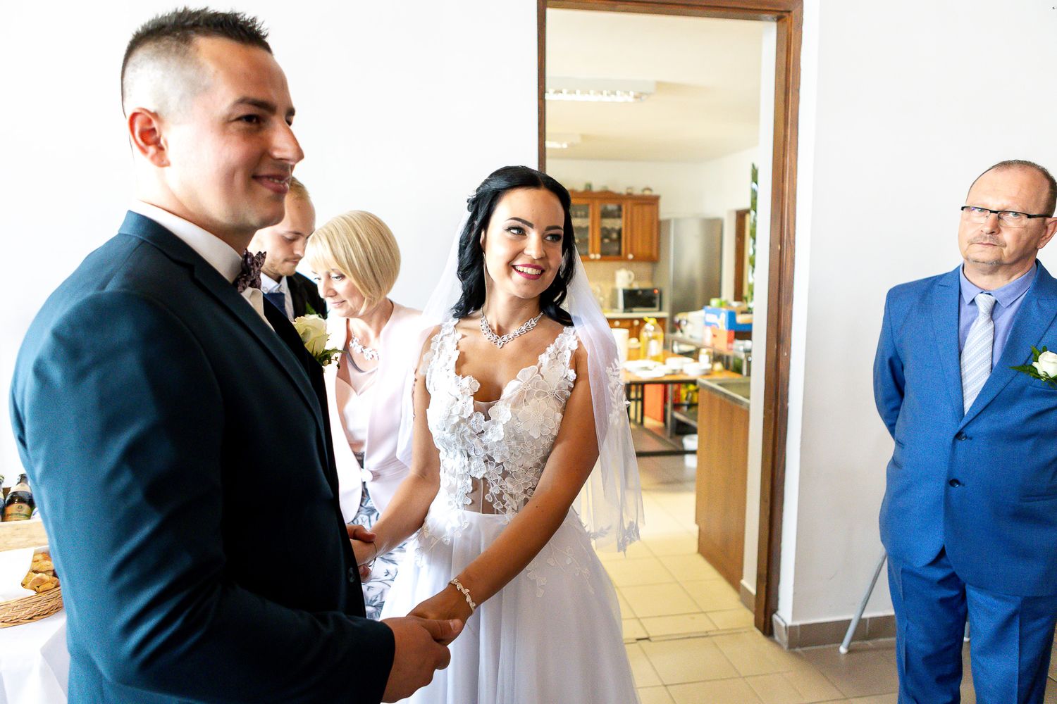 Wedding guests and bridal party members gather in a bright indoor hallway for candid moments and conversations.