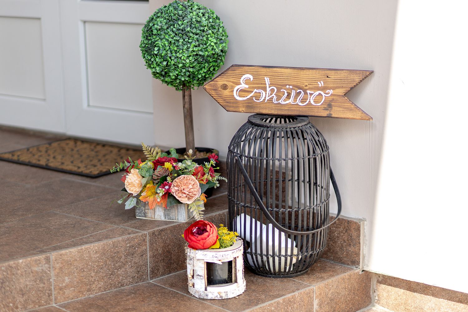 Decorative outdoor doormat and potted plants arranged near a rustic wooden door with hanging lantern decor.