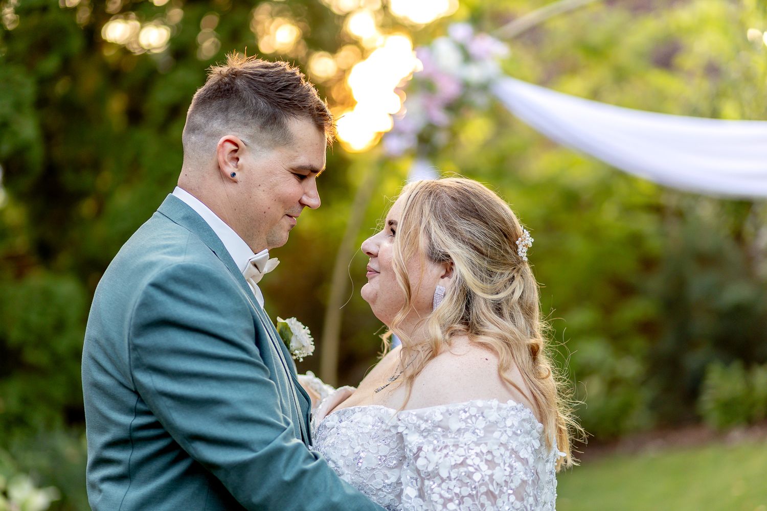 Bride and groom share an intimate moment in a garden setting under evening light.
