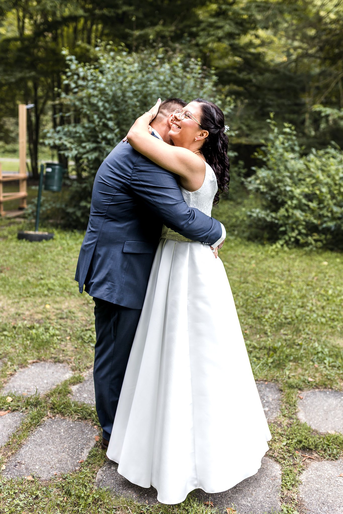 A couple in wedding attire embraces outdoors in a garden setting during their special day.