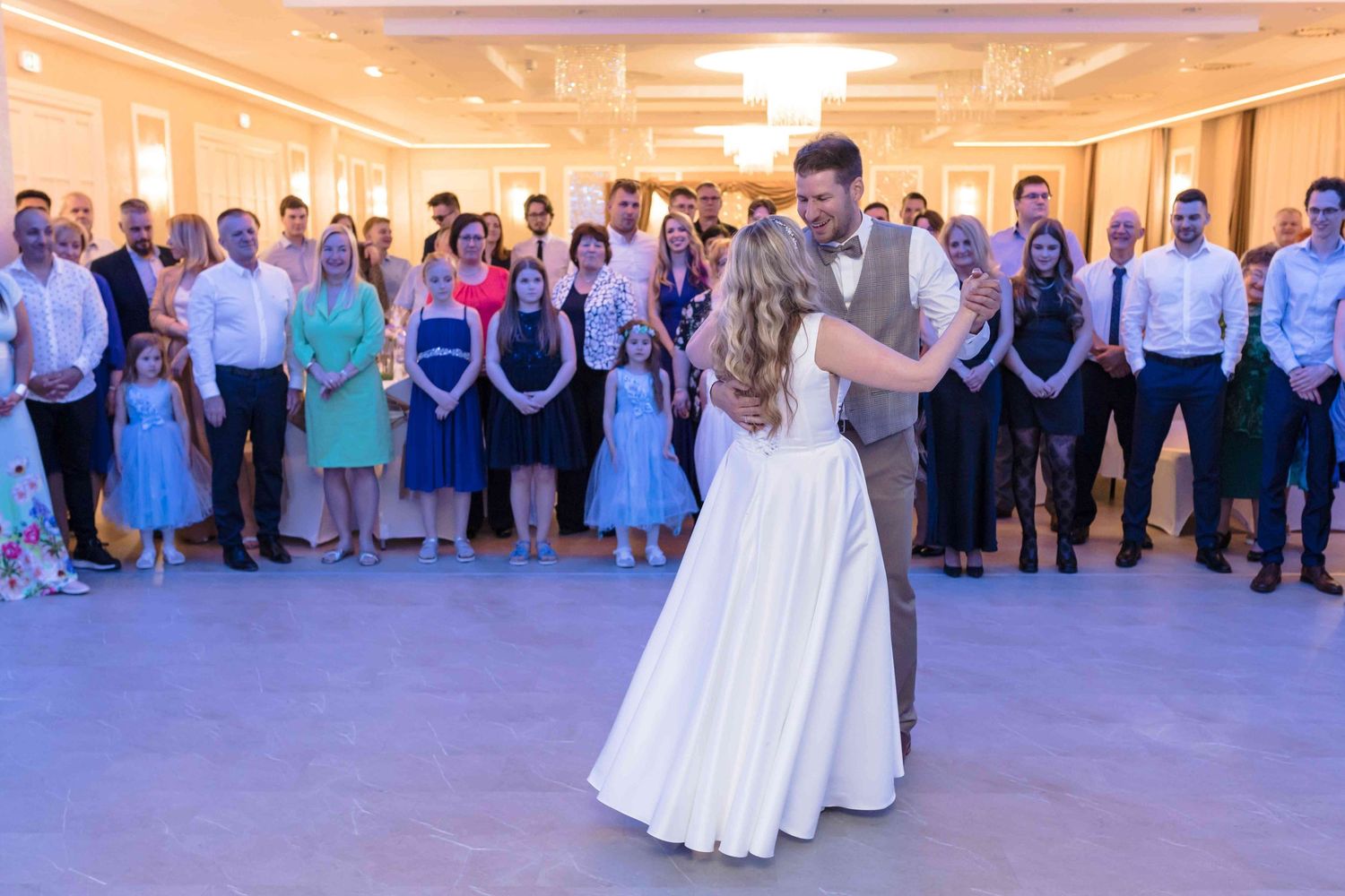 Wedding guests watch a couple dancing during a sunset reception in an outdoor courtyard setting.