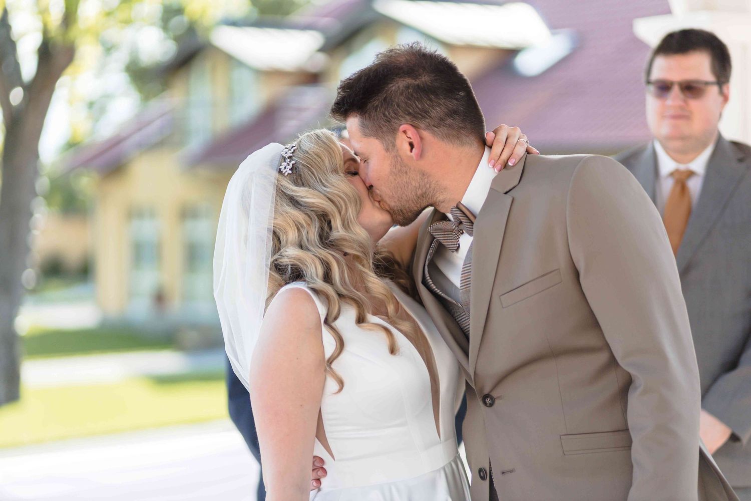 Wedding party members share a lighthearted moment during outdoor celebration in formal beige and gray attire.