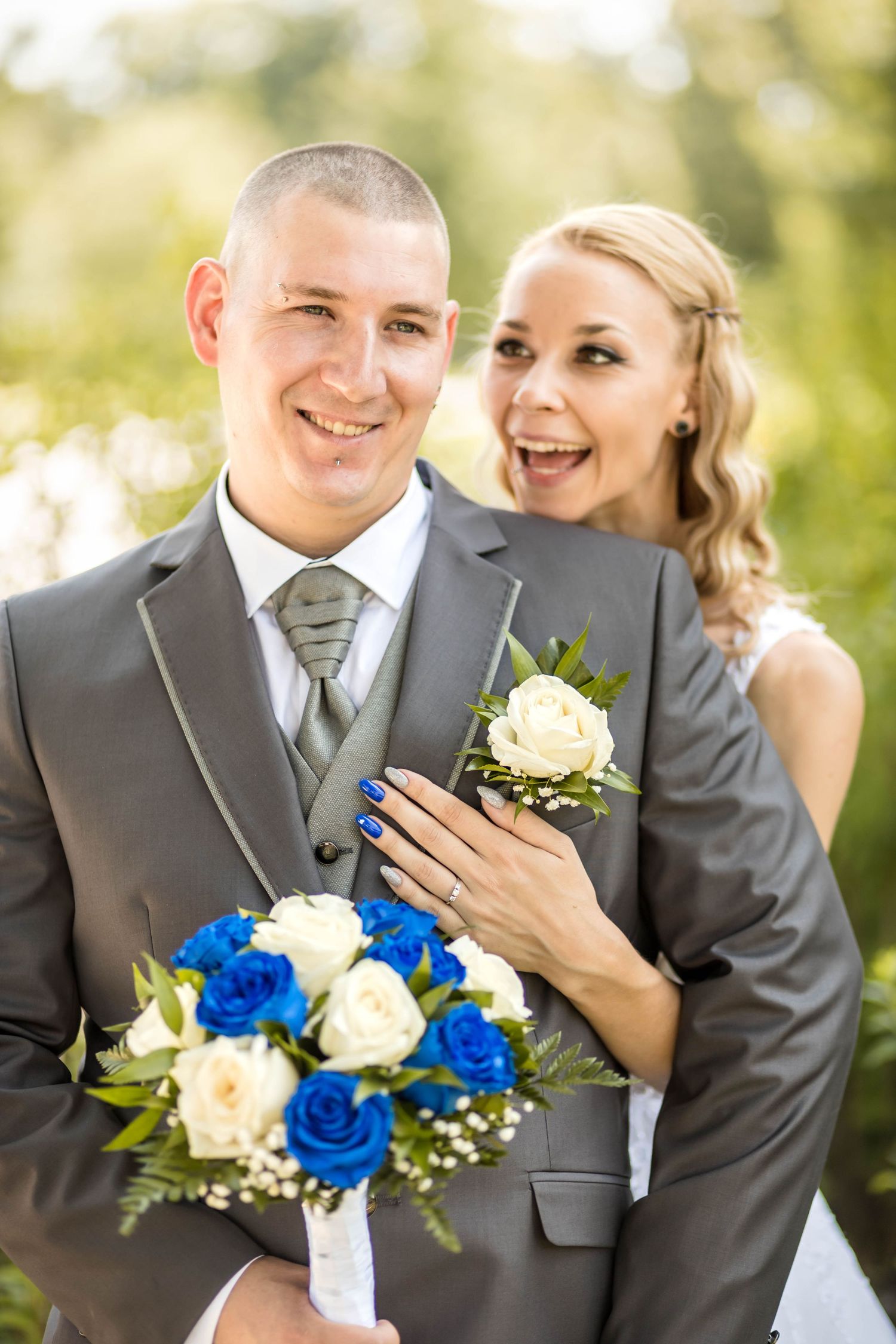 A joyful wedding couple shares a candid moment outdoors with a bouquet of blue and white roses.