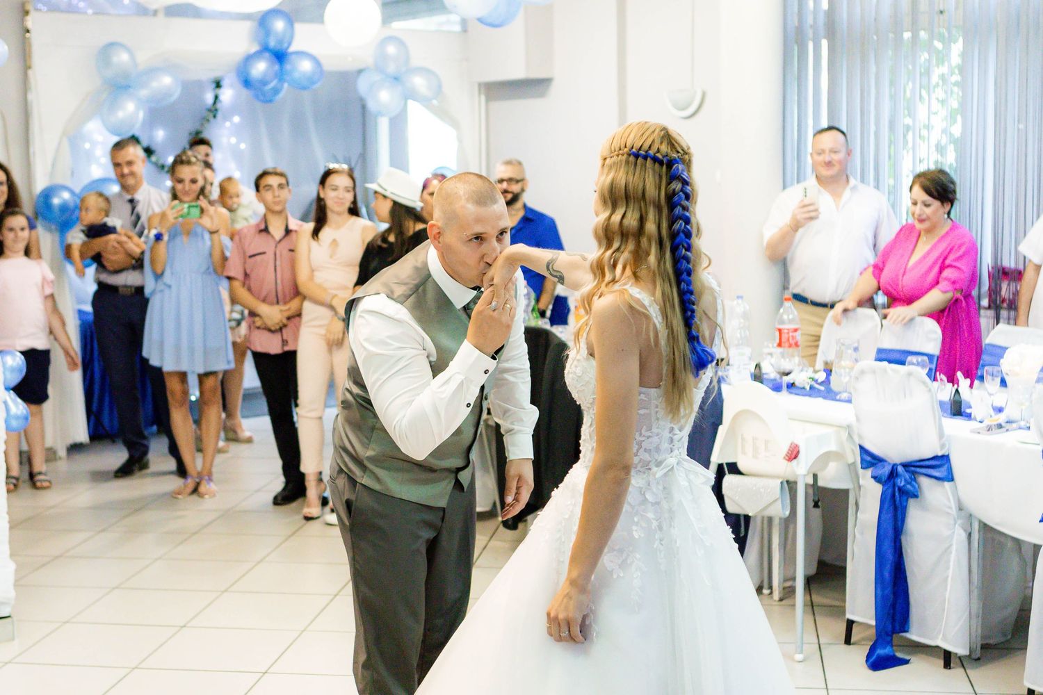 Wedding guests dance and celebrate together at a reception in a bright white venue decorated with blue accents.