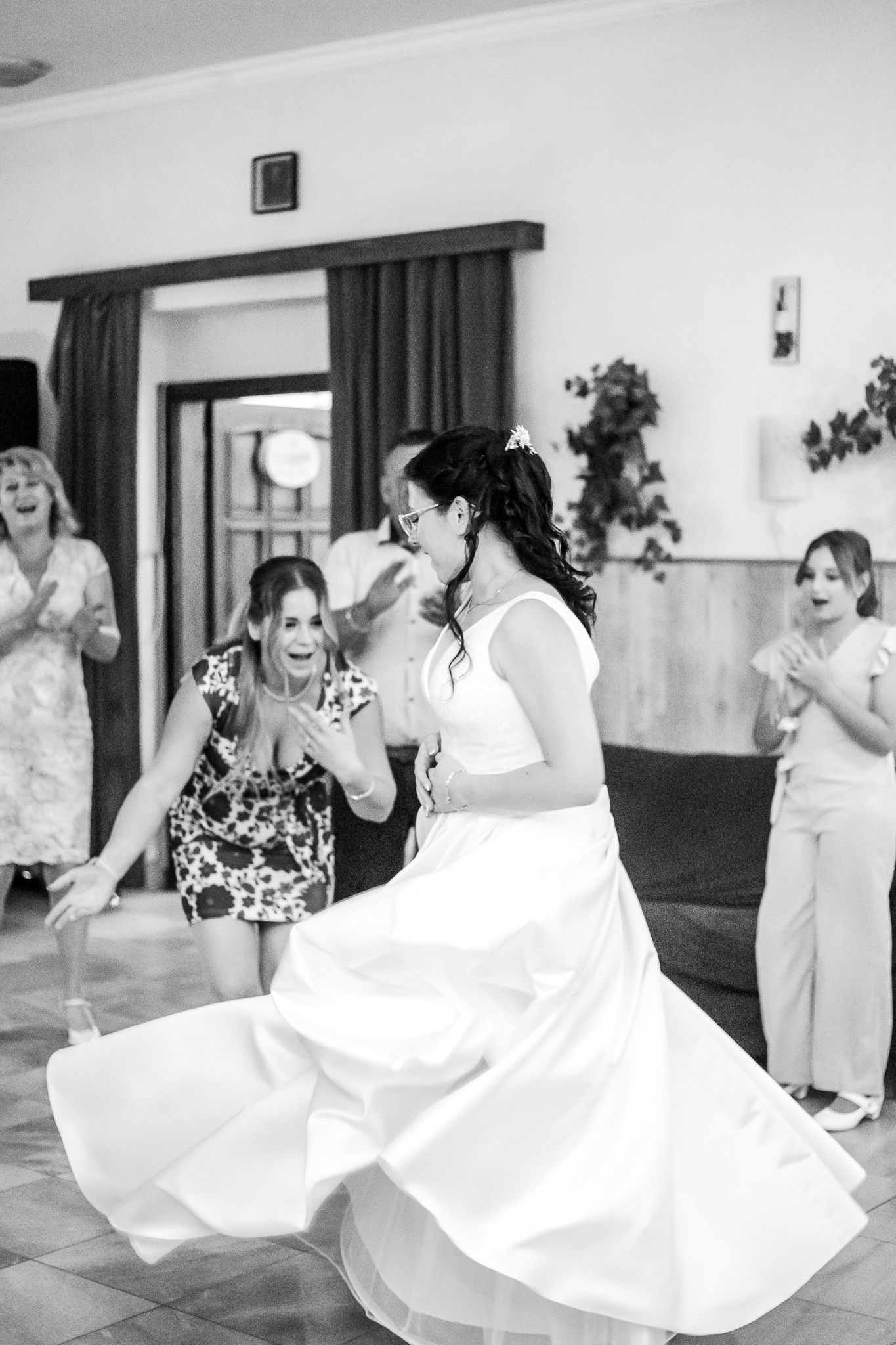 Wedding guests dance and twirl in a reception hall while a bride spins her white dress on the dance floor.