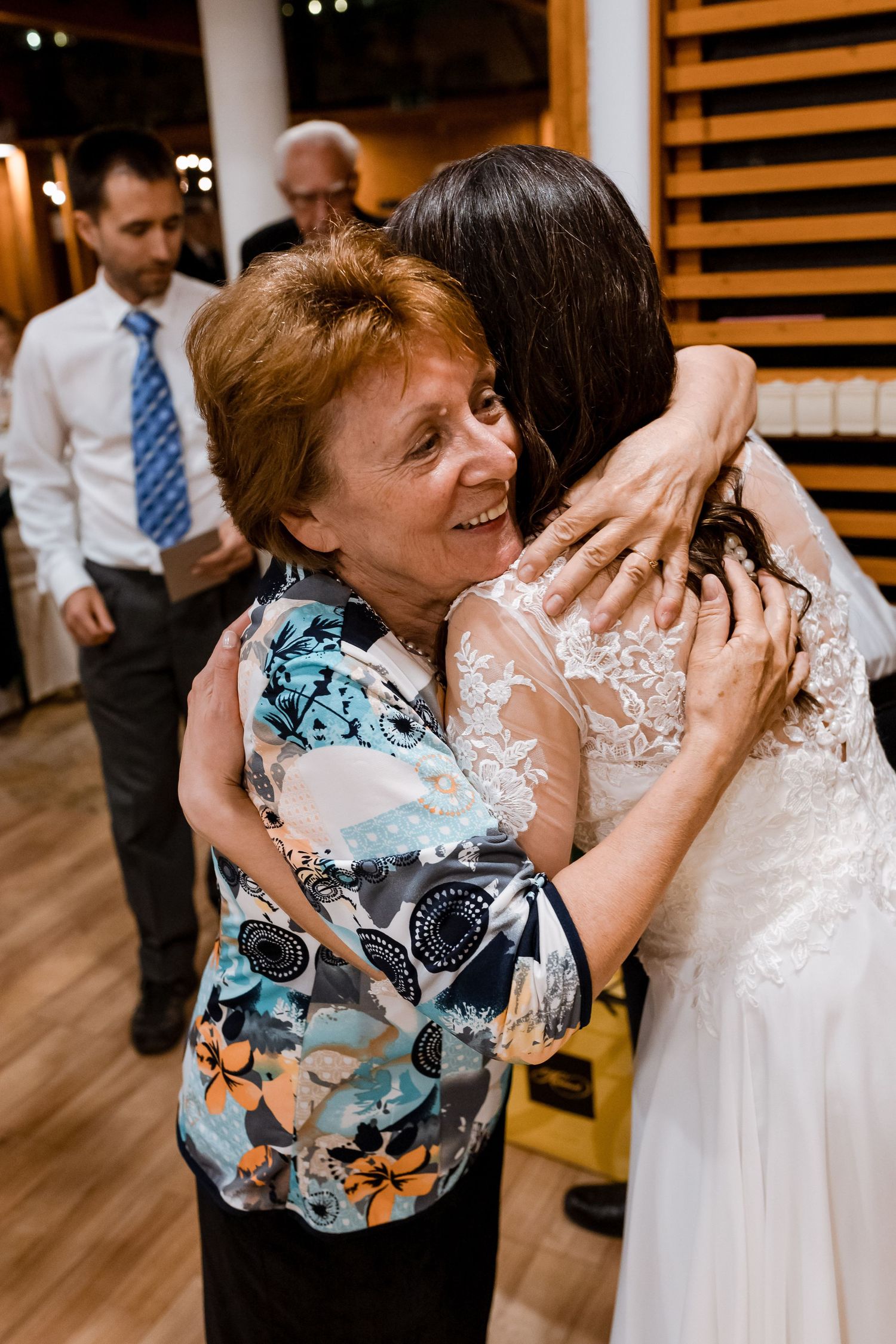 A series of candid wedding photos showing an emotional embrace between a guest in a blue floral dress and the bride.