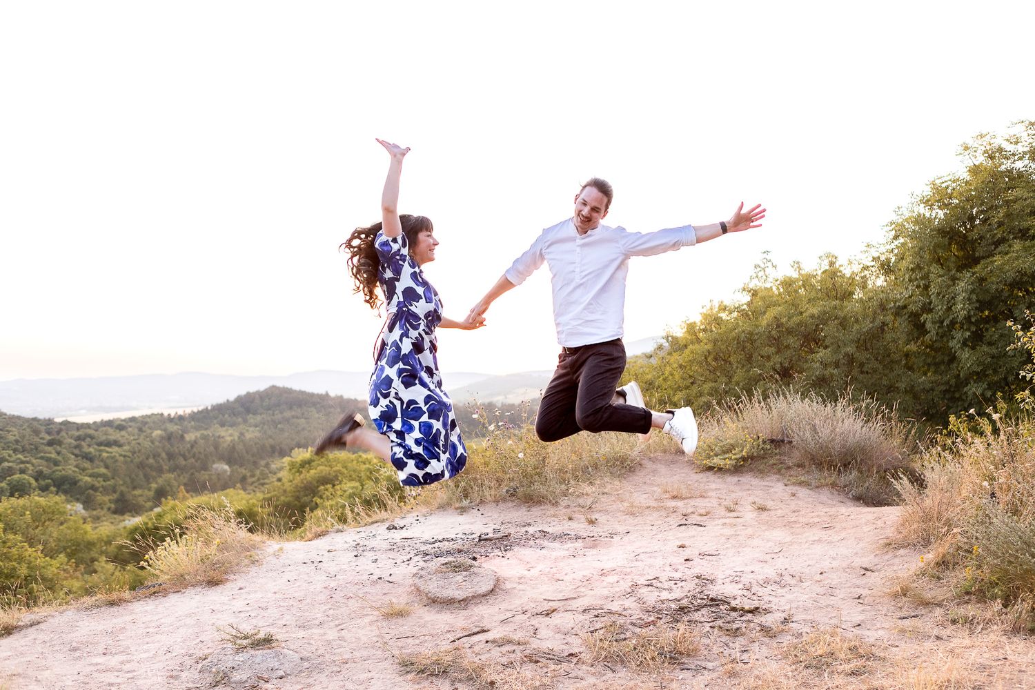 Couple embraces playfully on a scenic mountain trail during golden hour sunset.