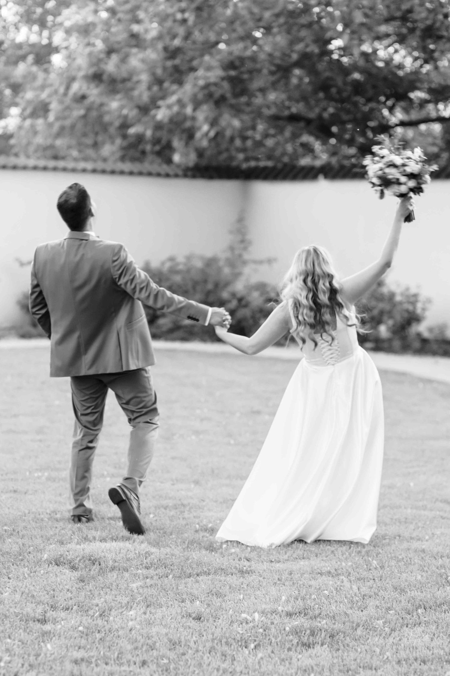 Black and white photo series showing a couple running and dancing playfully together on a grassy lawn.