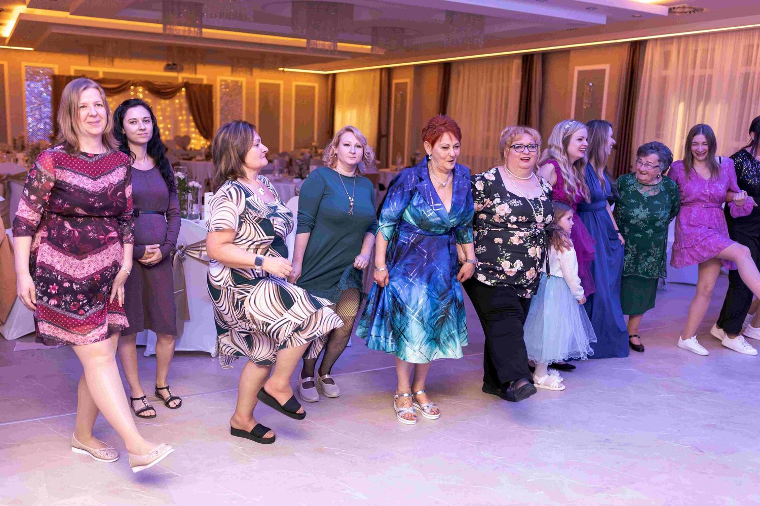 A group of people dancing in a line at a formal event with purple lighting and elegant decor.
