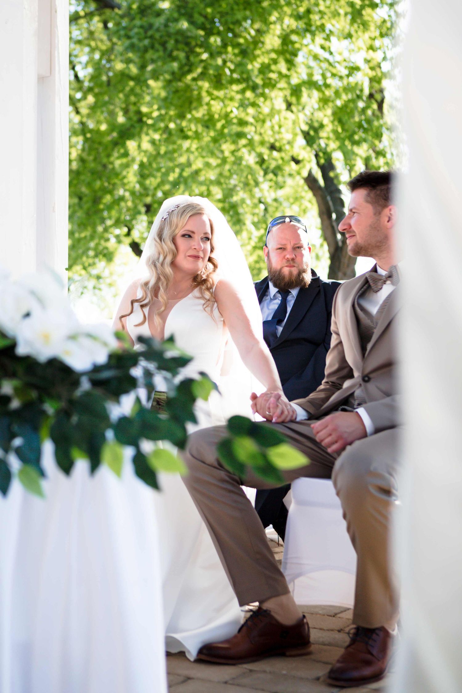 Romantic wedding moment captured through white columns showing couple sitting together on outdoor porch steps.