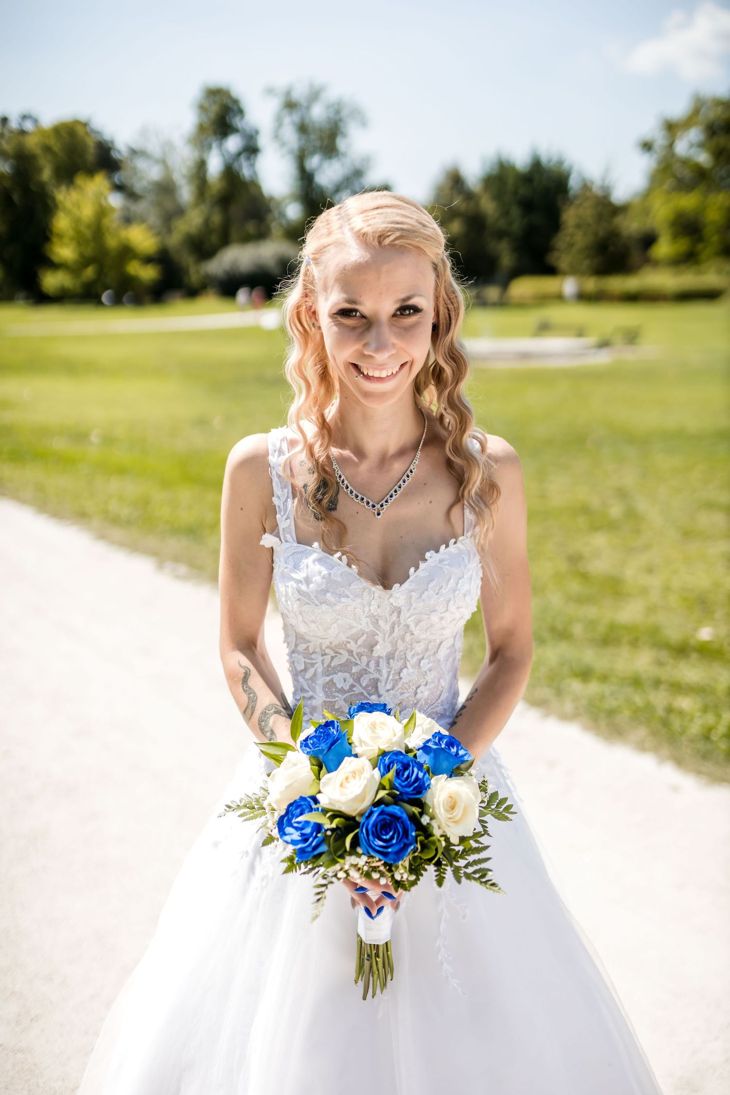 Beautiful wedding bouquet with vibrant blue and white flowers held against a white lace dress in outdoor setting.