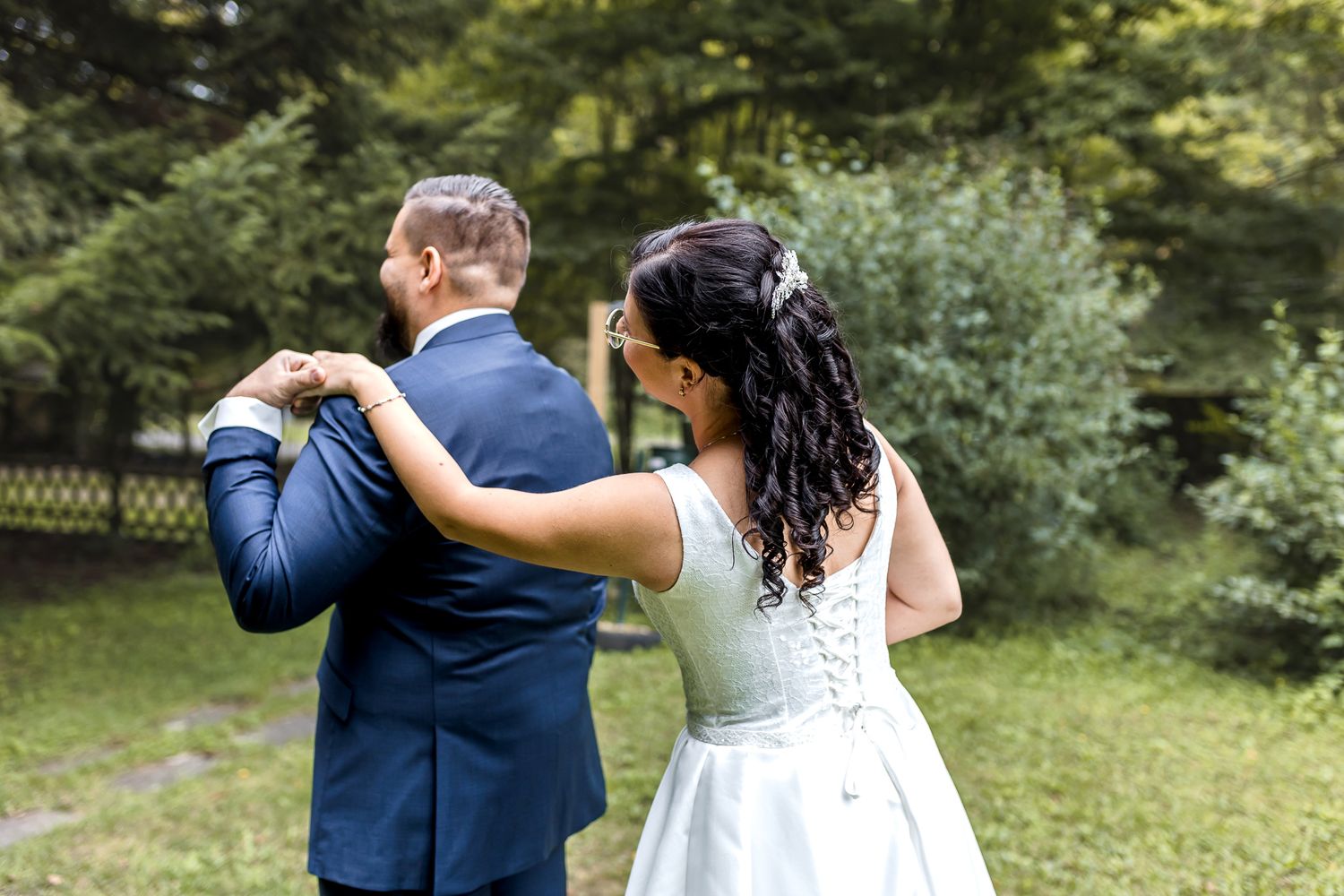 Couple in wedding attire embraces while walking through a lush garden setting during their special day.