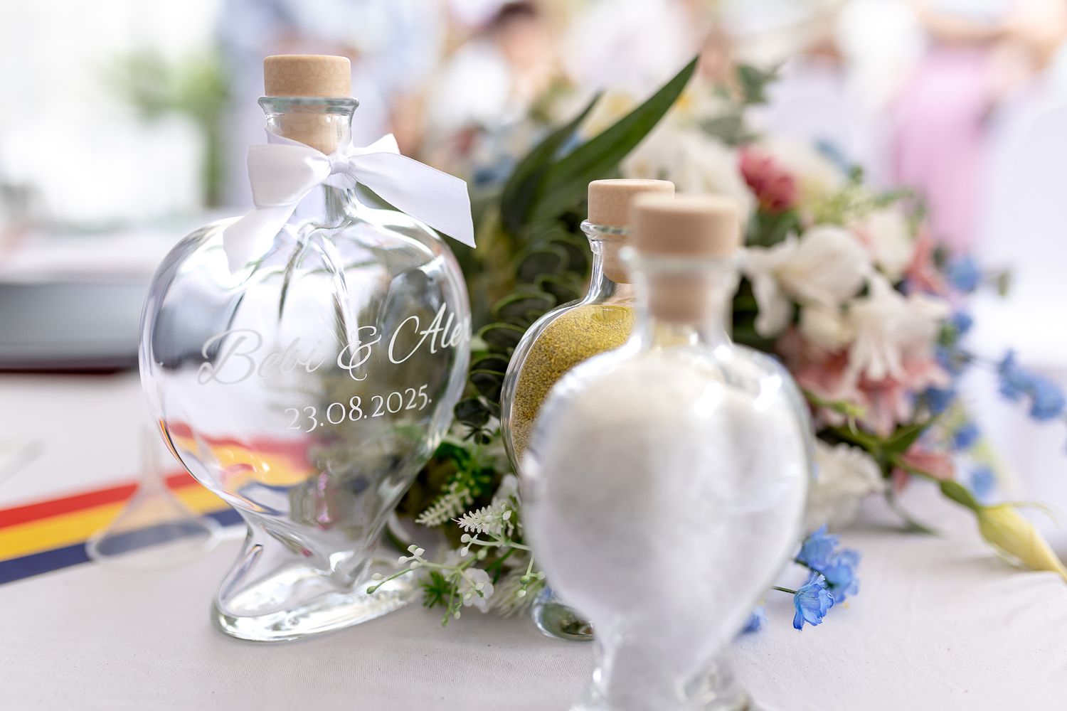 Elegant glass bottles with cork stoppers arranged with delicate flowers and ribbons on a white surface.
