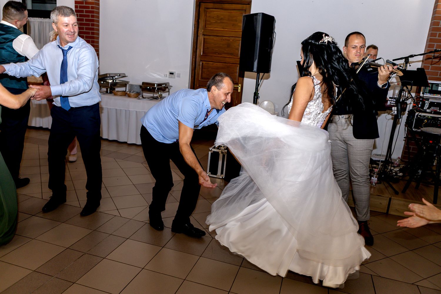 Dancers twirl across a reception hall floor as a band performs in the background during a wedding celebration.