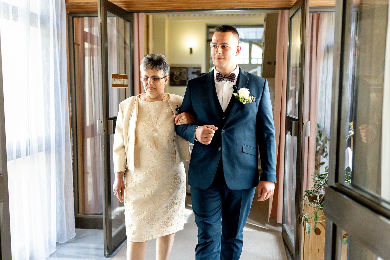 A couple walks arm in arm down an elegant hallway with wooden paneling and soft lighting.