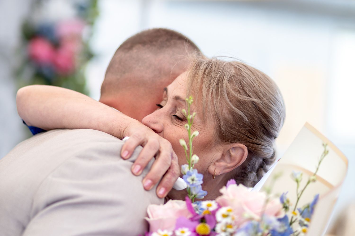 Couple shares a romantic kiss during an outdoor wedding ceremony surrounded by pink and purple flowers.