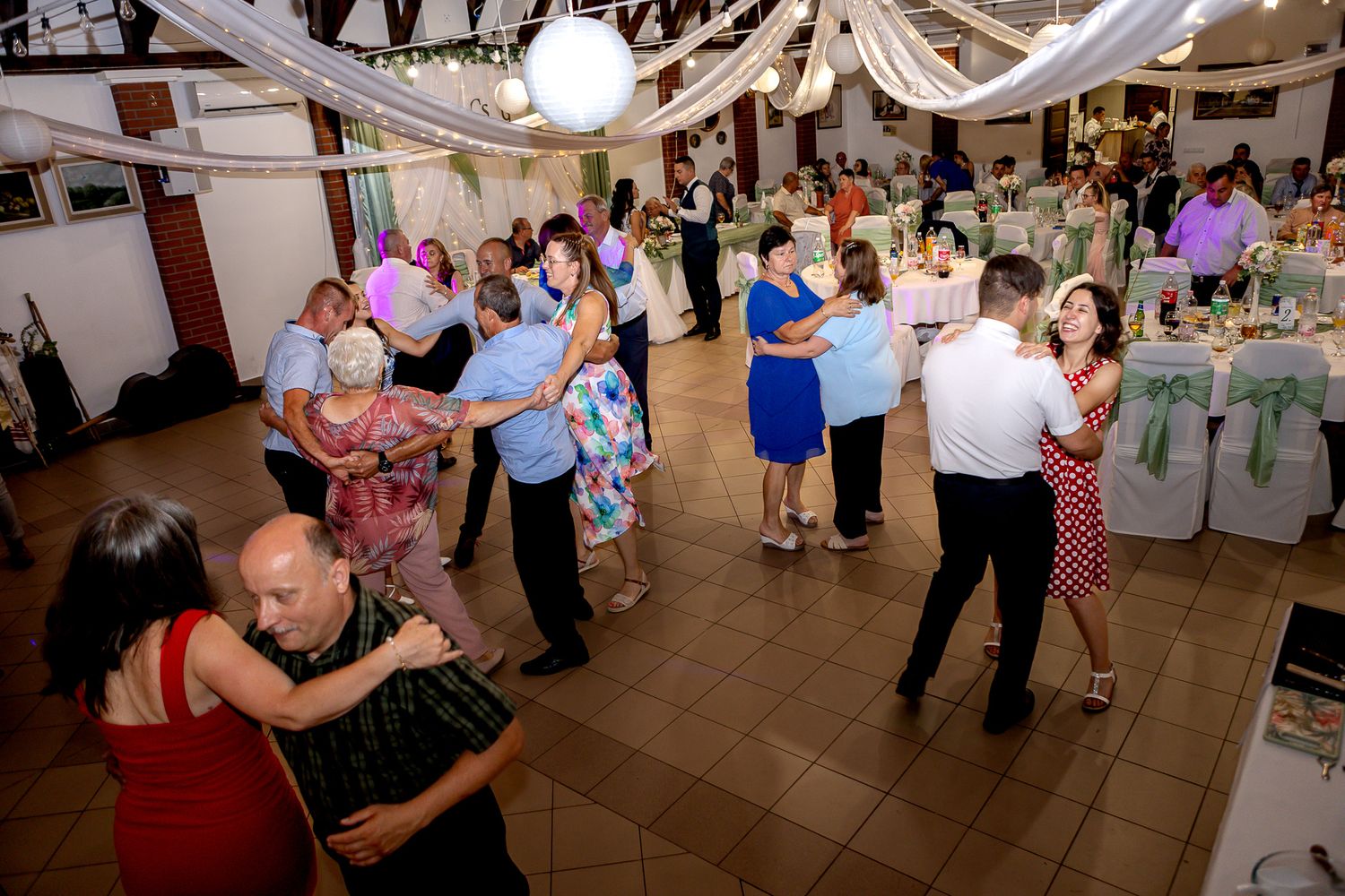 Wedding reception guests dancing and celebrating on a dance floor decorated with white streamers and party lights.