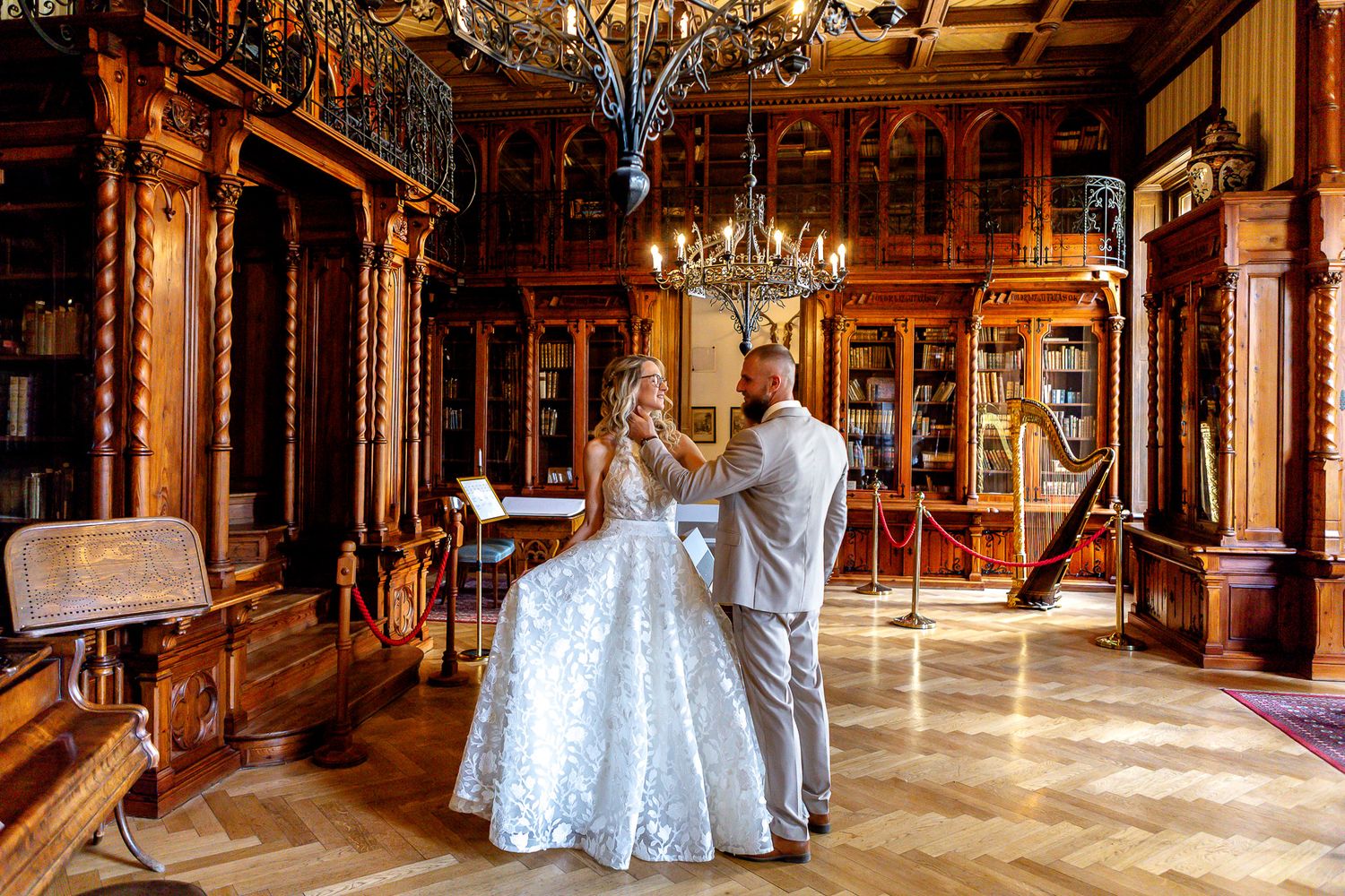 Elegant wedding reception venue with ornate chandeliers, wooden beams, and couples dancing on a polished wooden floor.