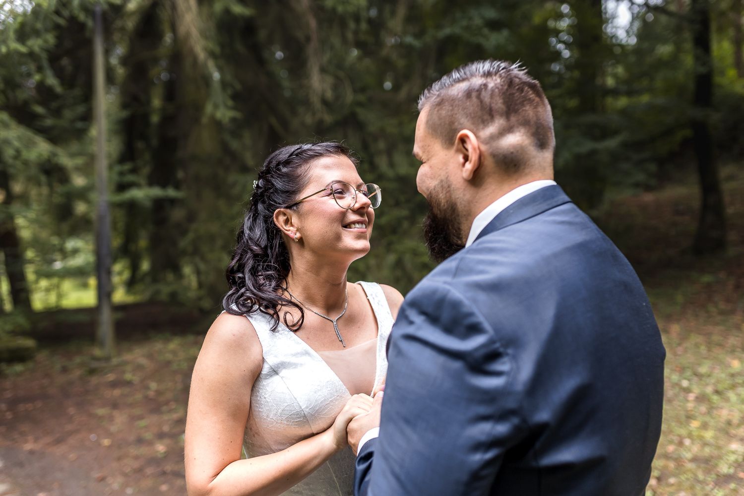 A couple shares a joyful moment together in a wooded outdoor setting during their wedding day.