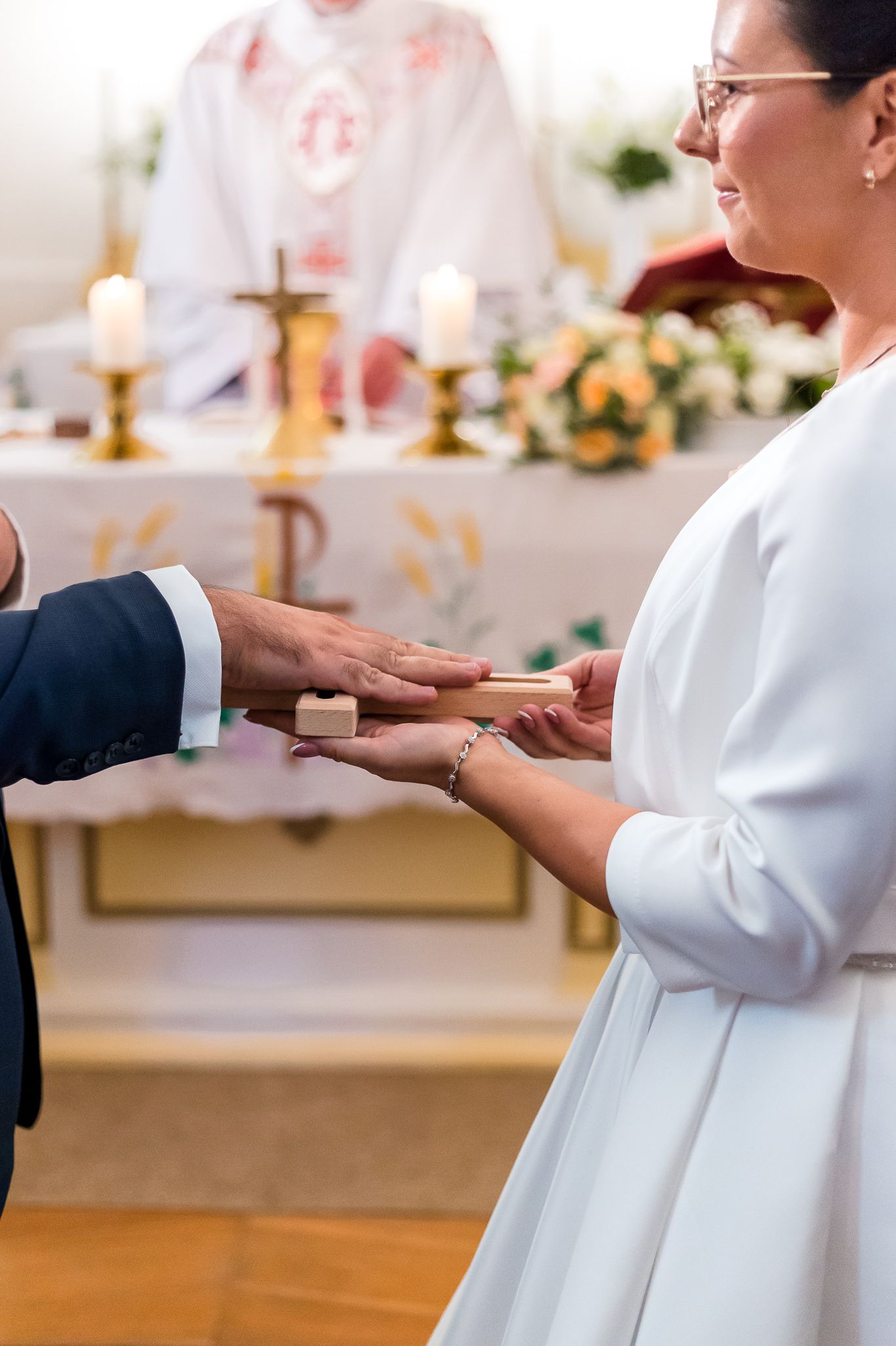 Close-up of hands exchanging wedding rings during a traditional church ceremony with candlelit altar in background.