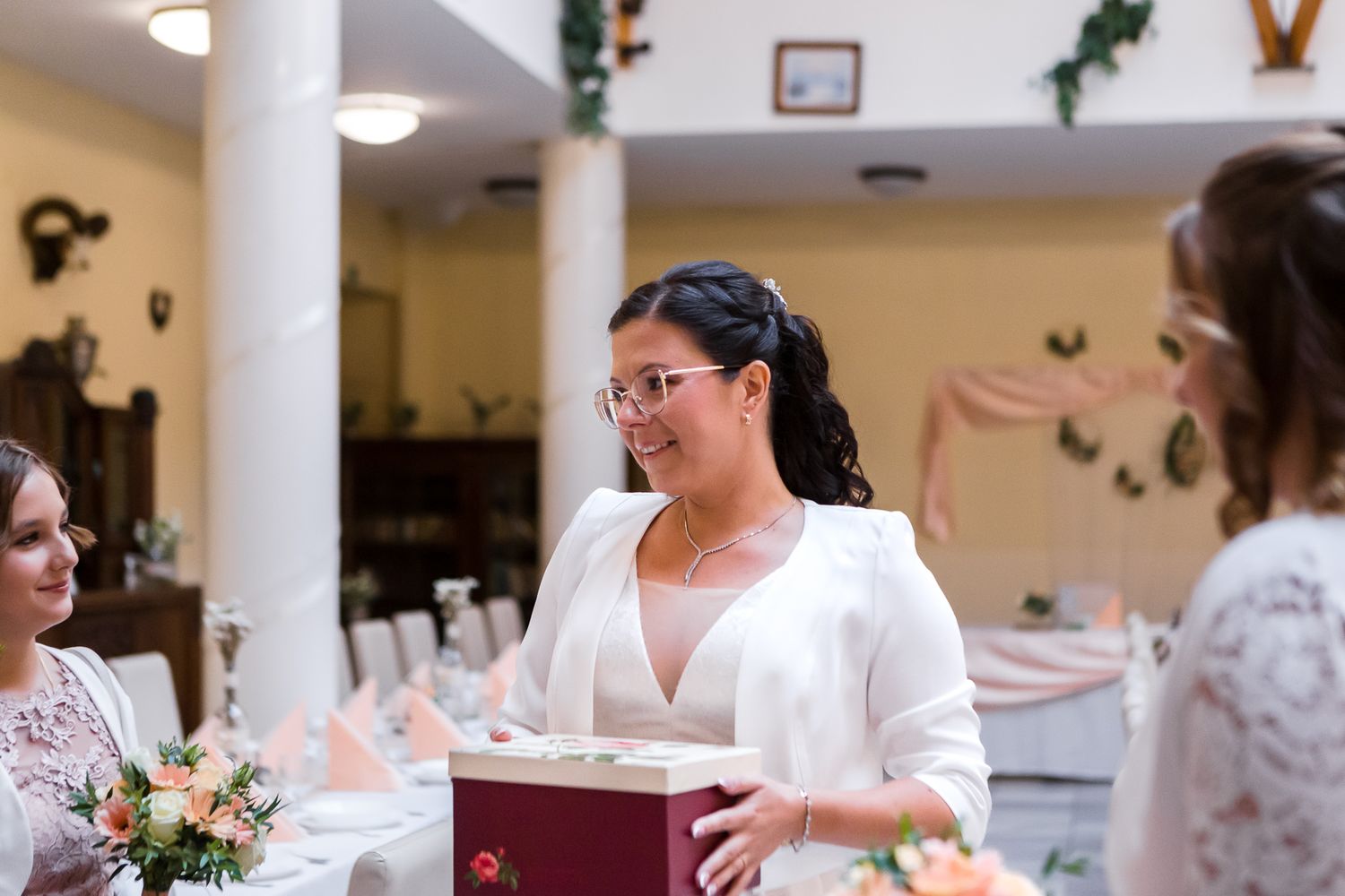 Wedding party members in white dresses prepare for a celebration in an elegant indoor venue.