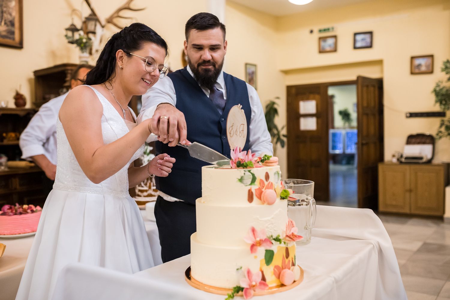 A wedding reception venue shows guests enjoying a cake cutting ceremony at a rustic banquet hall.