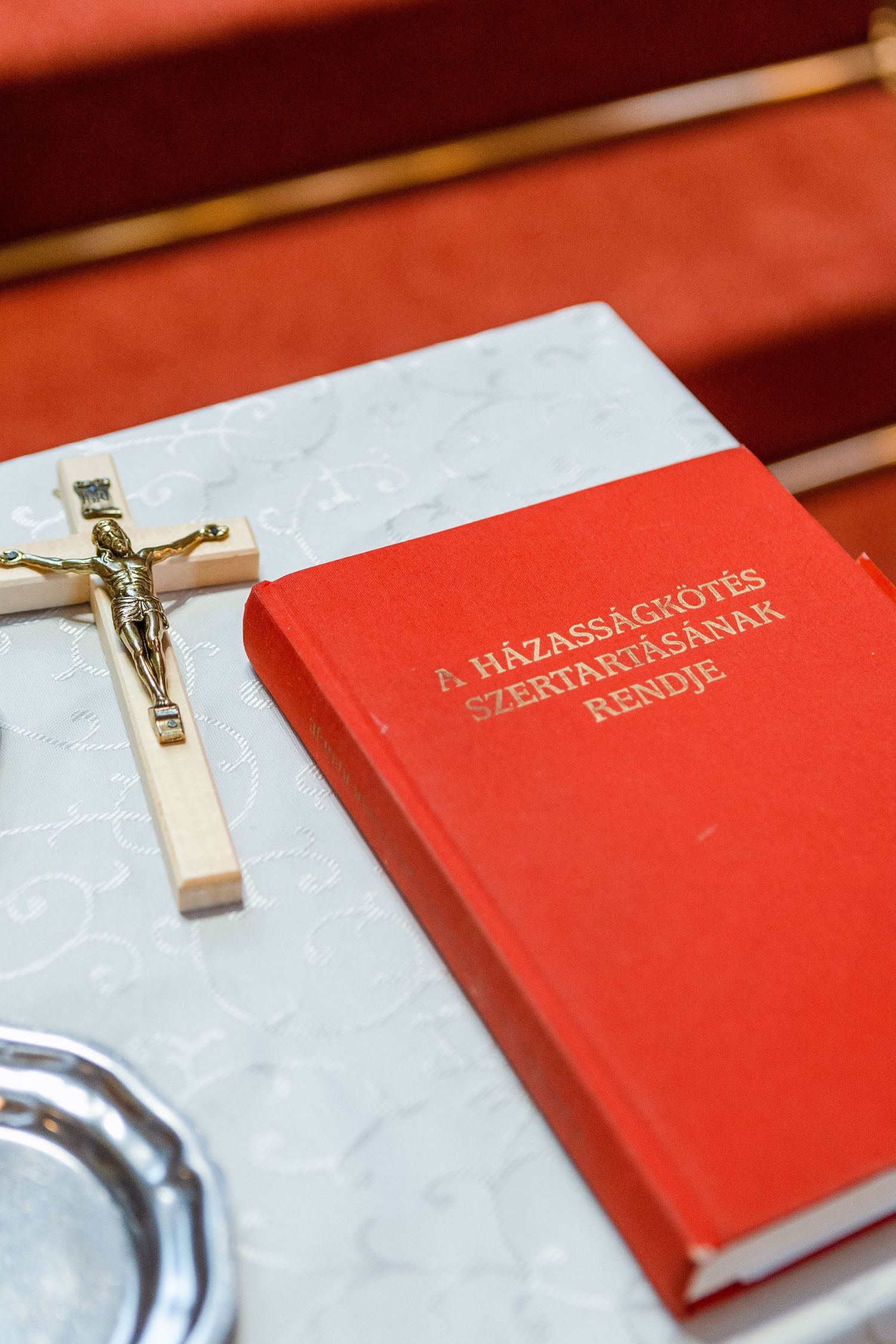 Red leather-bound prayer book with gold lettering and crucifix lying on white marble surface.