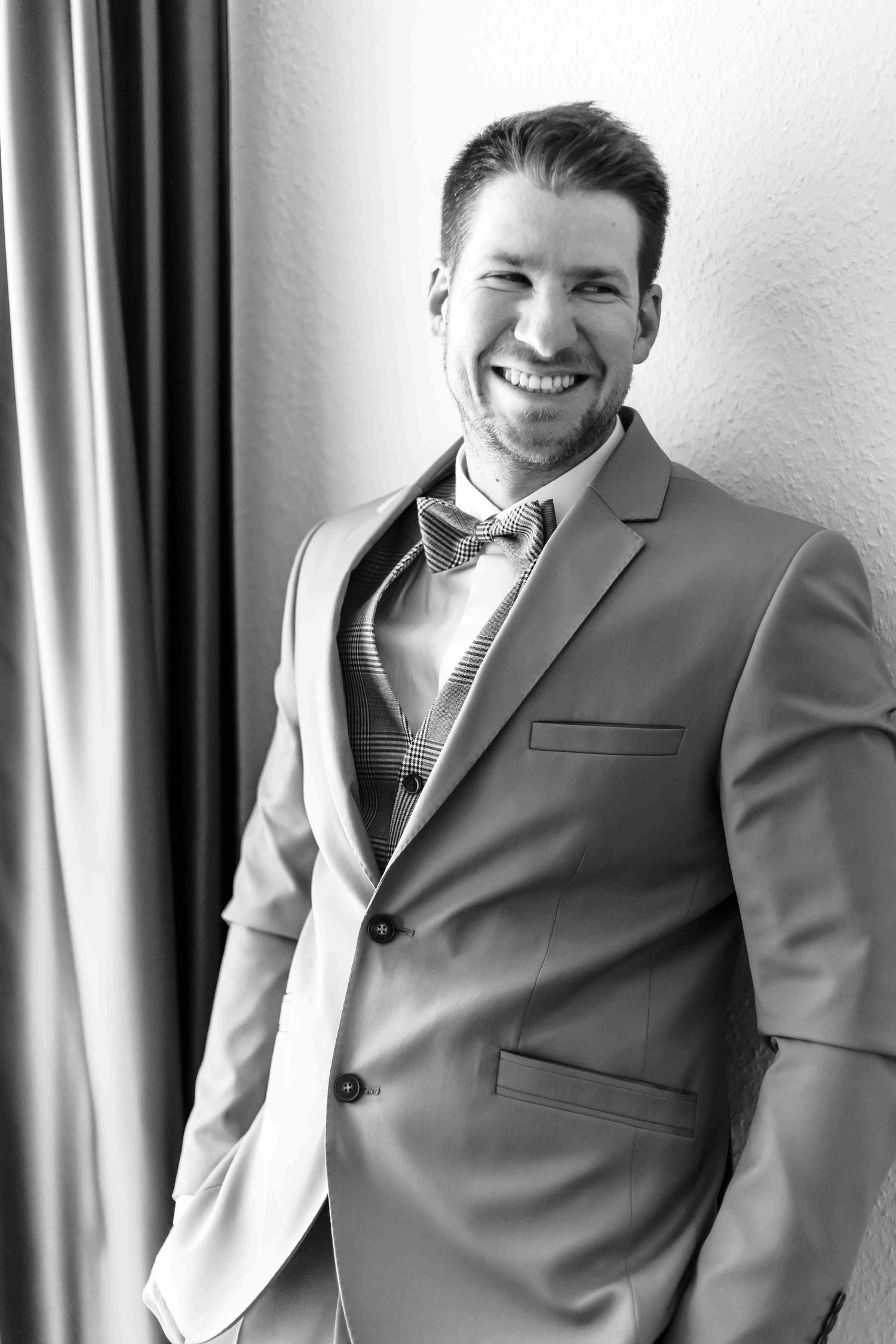 A black and white photo series showing someone in a gray suit jacket smiling and posing against a wall.
