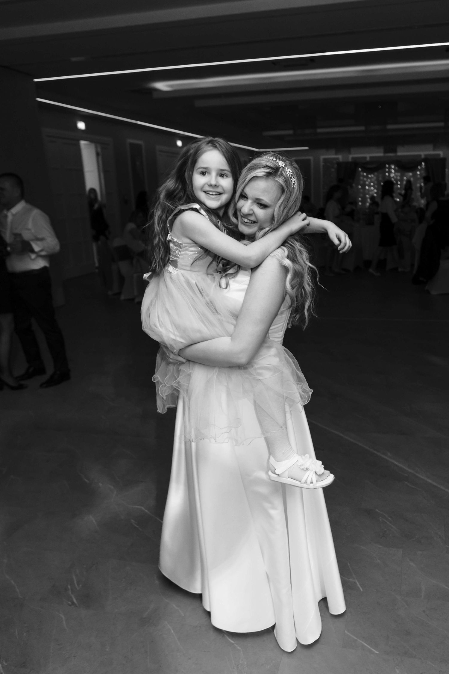 A tender moment captured in black and white as two people in white dresses embrace on a dance floor.