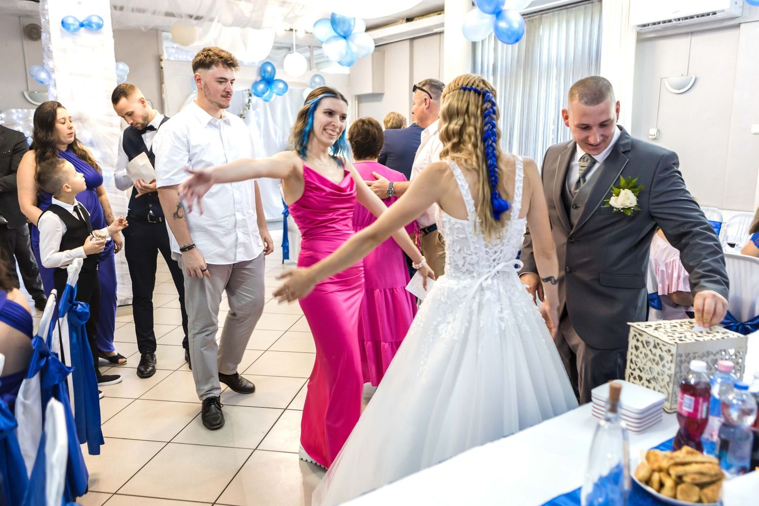 Wedding celebration with guests dancing and mingling at a reception decorated with blue and white balloons.