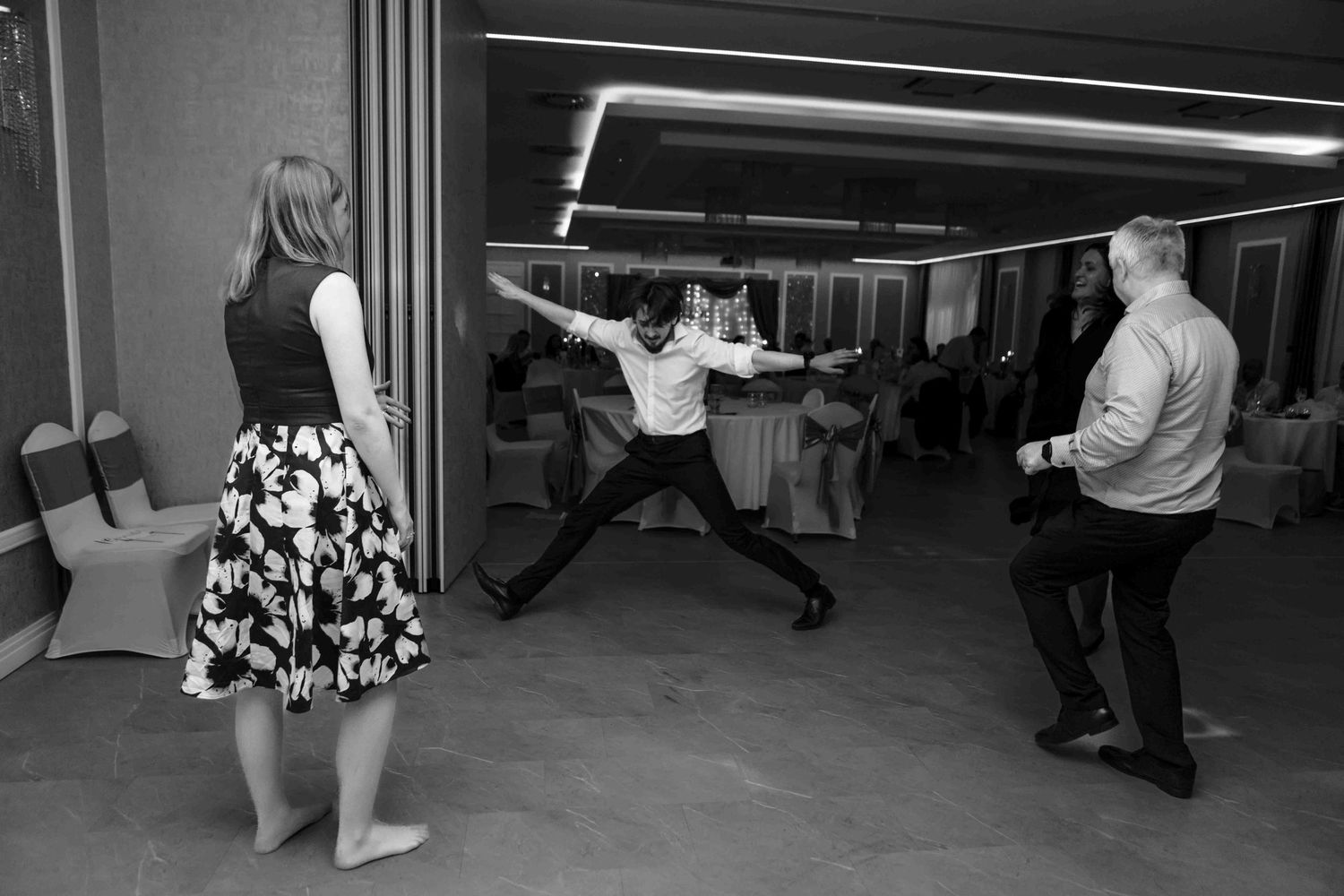 A black and white photo of a dance studio with multiple people practicing ballet positions at the barre.