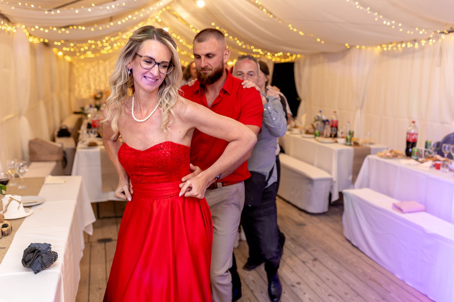 A couple in formal attire dance together at an elegant wedding reception with white drapes and golden lights.