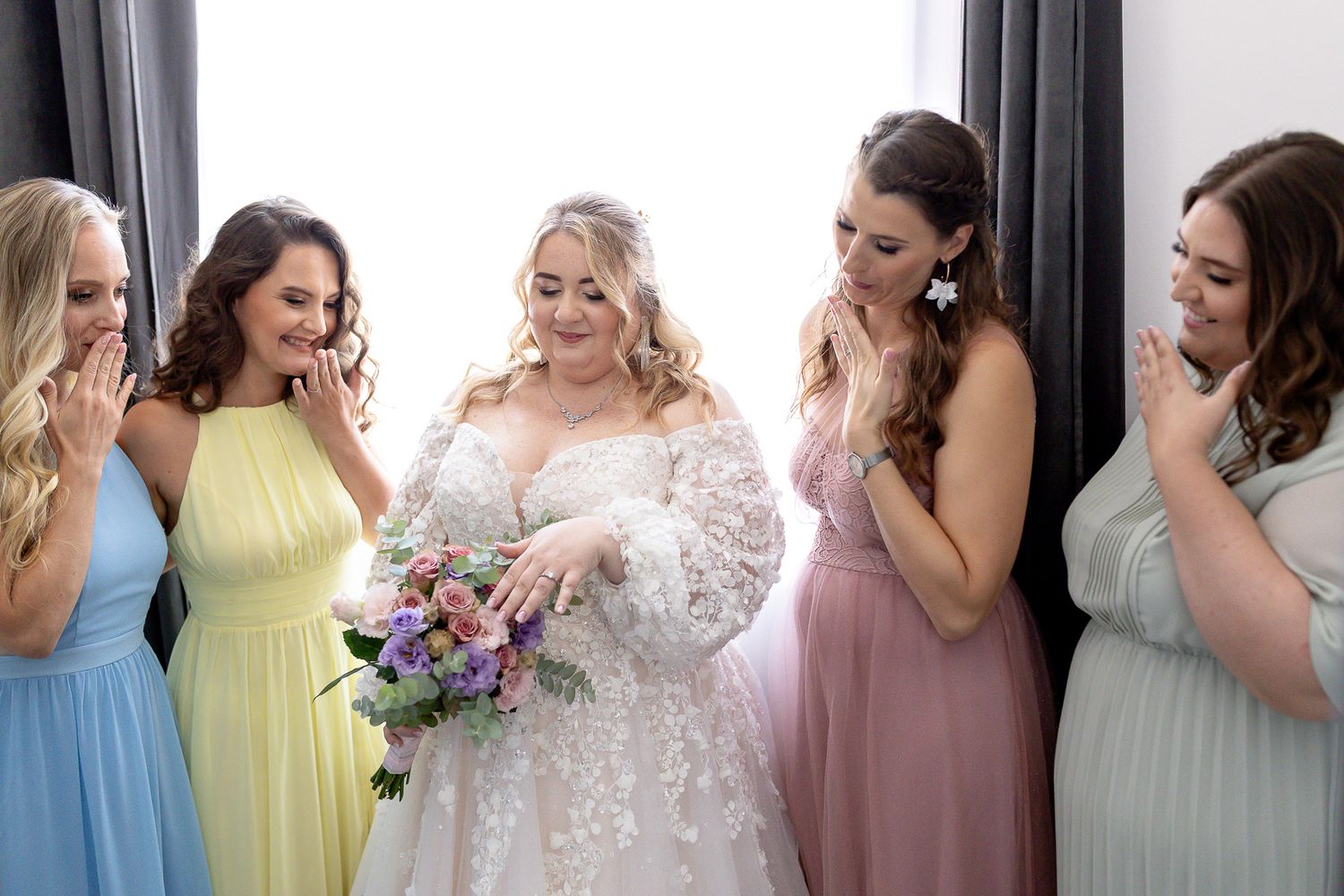 A row of bridesmaids in pastel dresses stand together during a wedding celebration.