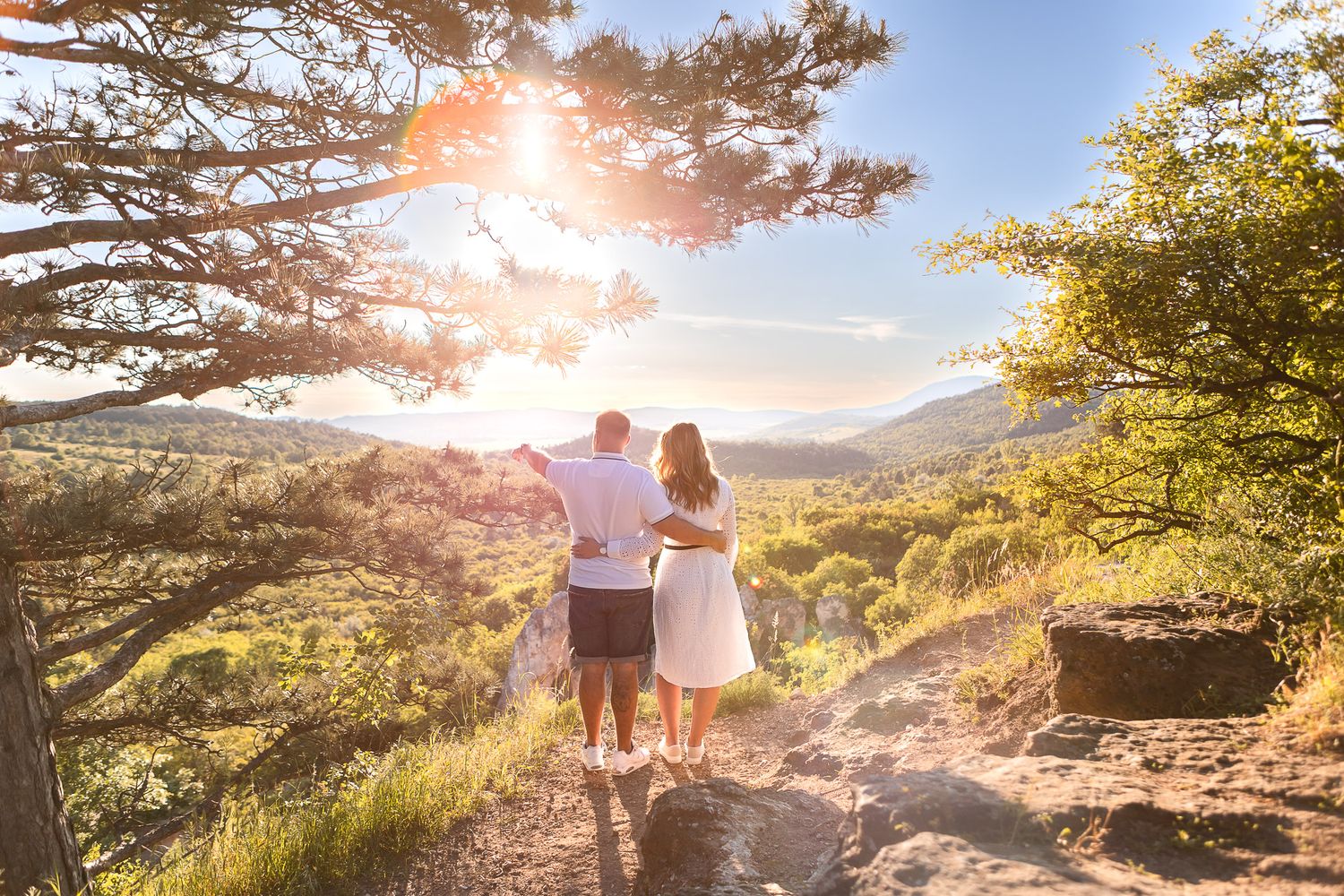 Sun flare illuminates couple walking along mountain path during sunset.