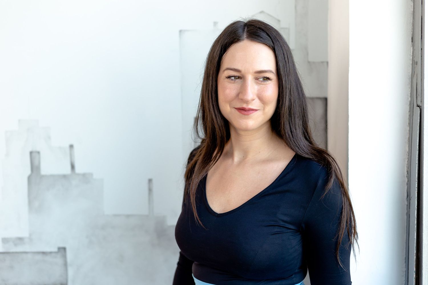 A person in a black top poses confidently against a minimalist white background.